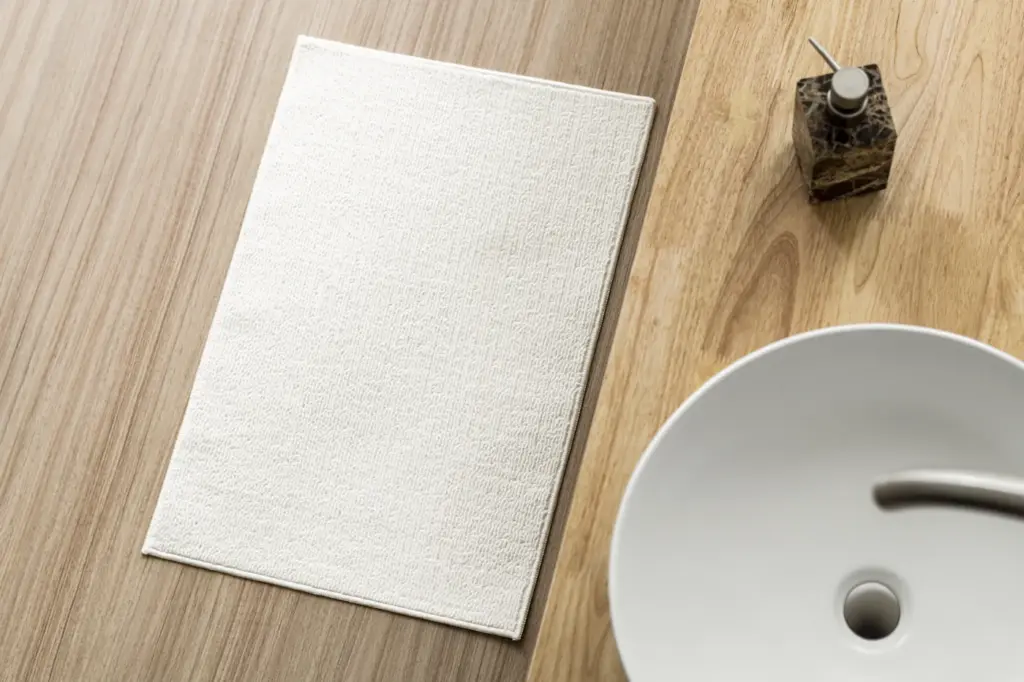 A white bath mat on a timber floor beside a basin