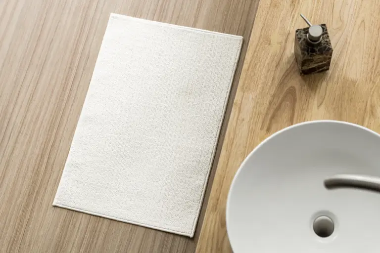 A white bath mat on a timber floor beside a basin