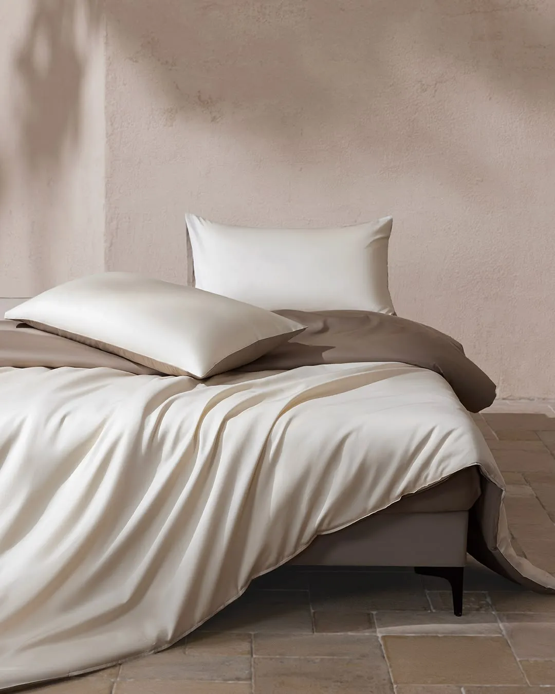 Bed made with crumpled white and taupe linen